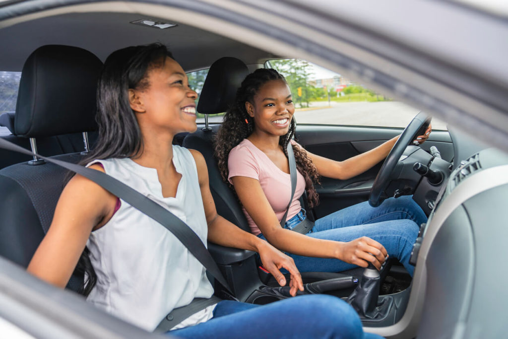Mom in the passenger seat with daughter driving, both smiling