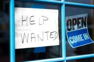 A photo of a help wanted sign in the window of a store.