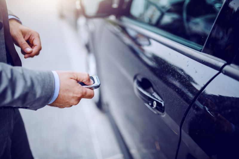 A photo of a man holding a key fob next to a vehicle.