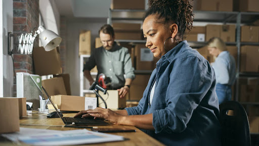 Business owner managing inventory and orders on a laptop in a warehouse, emphasizing the need for commercial insurance to protect operations in Ontario