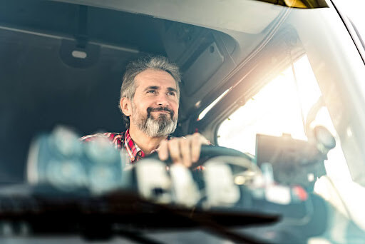 Smiling truck driver in a commercial vehicle, highlighting the need for commercial vehicle insurance in Ontario.